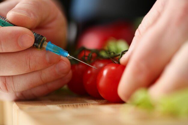 Homem fazendo uma injeção em um close de mãos de tomate vermelho