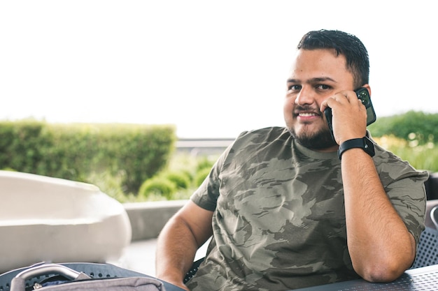 Homem fazendo uma ligação de seu smartphone. Jovem colombiano usando seu telefone enquanto está sentado em uma cadeira.