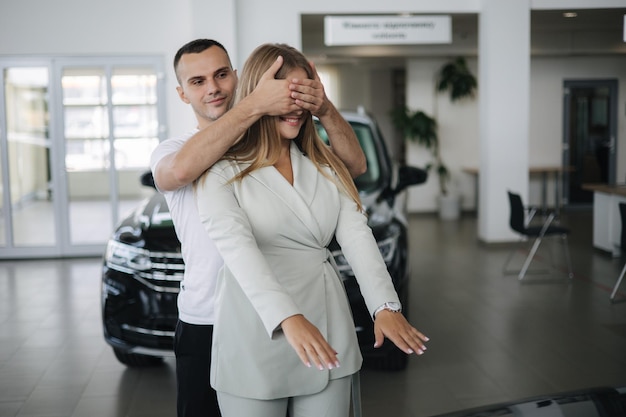 Homem fecha os olhos para sua esposa e faz uma surpresa comprando carro homem e mulher no showroom de carros feliz jovem