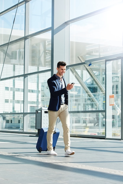 Homem feliz andando com mala e telefone no terminal