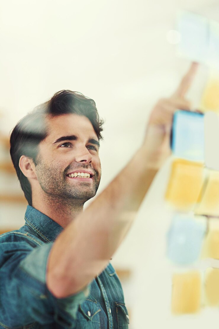 Foto homem feliz anota e planeja o horário com um quadro de vidro no escritório para brainstorming ou tarefas jovem homem ou empregado criativo com sorriso para lembrete visão ou agenda em startup no local de trabalho