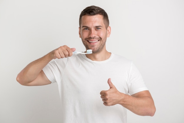 Homem feliz, aparecendo o polegar e segurando a escova de dente com pasta