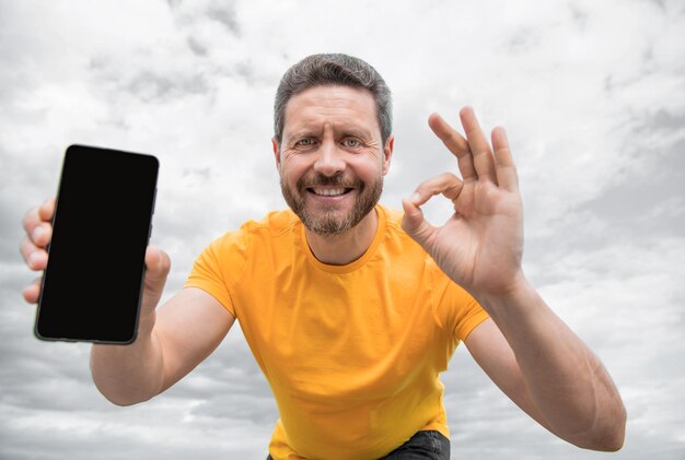 Homem feliz apresentando a tela do smartphone com espaço de cópia ok