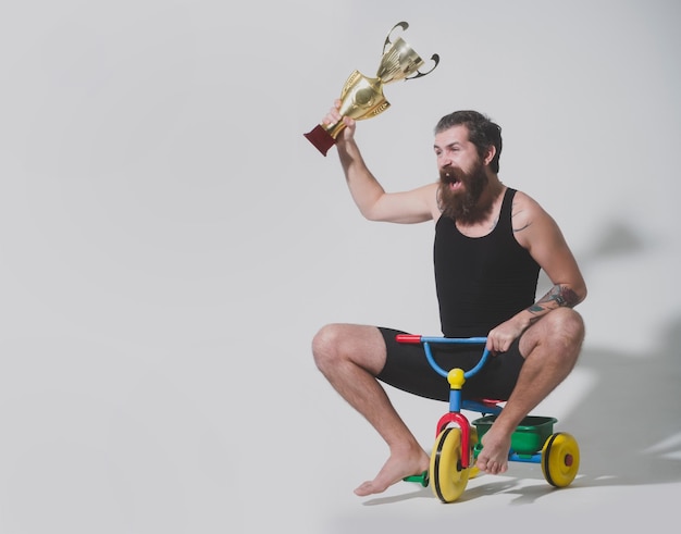 Homem feliz barbudo detém a taça de campeão de ouro no brinquedo de bicicleta