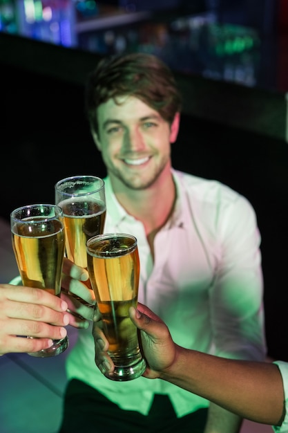 Homem feliz, brindando seu copo de cerveja com os amigos no bar