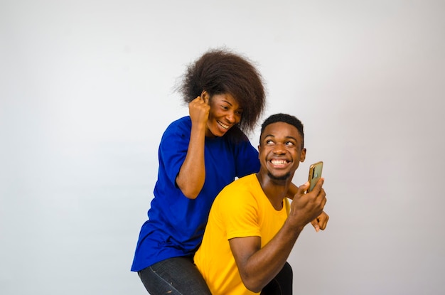 Homem feliz carregando sua namorada isolada sobre fundo branco, sentindo-se animado com o que ele está mostrando a namorada em seu telefone