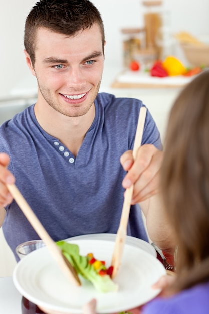 Homem feliz colocando salada em um prato jantando com sua namorada no ktichen