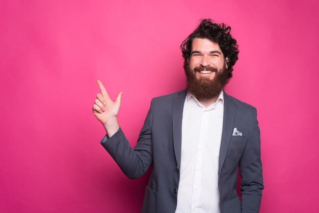 Homem feliz com barba casual sorrindo e apontando para copyspace