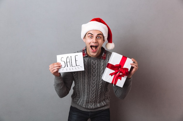 Homem feliz com chapéu de papai noel segurando um presente