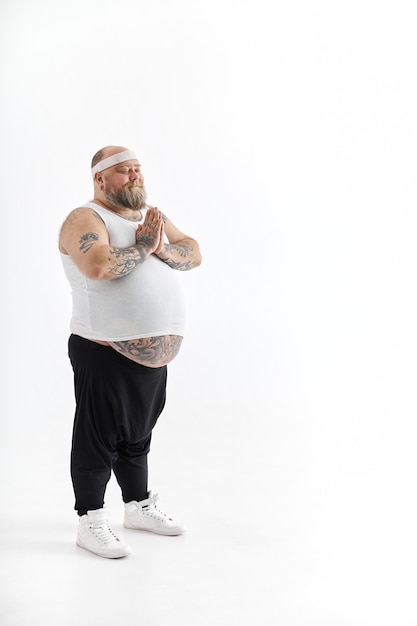 Homem feliz com excesso de peso, barriga grande e tatuagens em roupas esportivas, posando em fundo branco