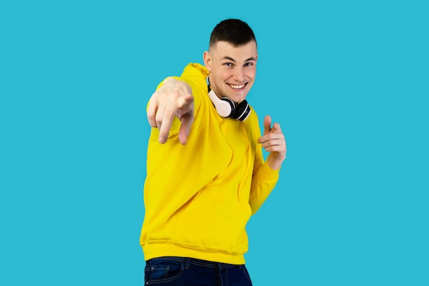 Homem feliz com fones de ouvido sem fio apontando para o fundo azul da câmera