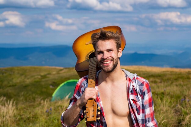 Homem feliz com guitarra no acampamento Sentindo-se livre e relaxado Caminhando aventura Homens com guitarra em camisa quadriculada