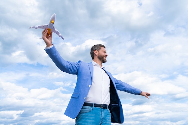 Homem feliz com o avião de brinquedo. sucesso nos negócios. homem de sucesso no terno sonhando. empresário pronto para a viagem. liberdade. chefe maduro com avião no fundo do céu. empresário confiante. ideia de voar.