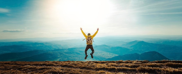 Homem feliz com os braços abertos pulando no topo da montanha