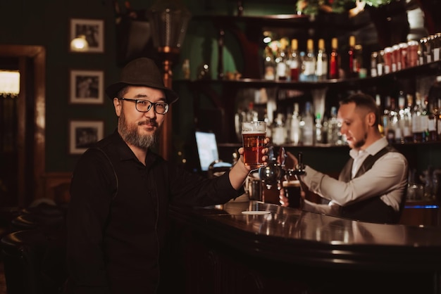 Homem feliz com um copo de cerveja na mão está descansando no balcão do bar