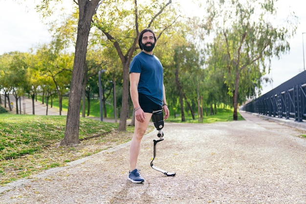 Homem feliz com uma prótese de perna esportiva posa em um parque mostrando resiliência