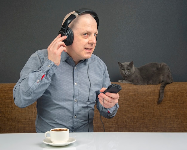 Homem feliz com uma xícara de café em fones de ouvido portáteis ouve música usando um player.