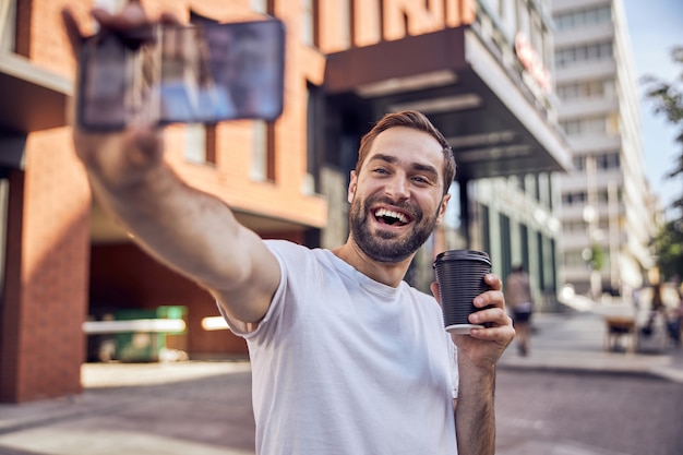 Homem feliz com uma xícara de café tira uma selfie de perto