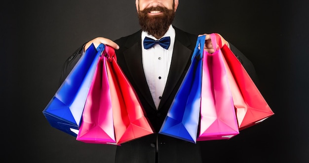 Homem feliz cortado em gravata borboleta de smoking em fundo preto com sacolas de compras dia dos namorados