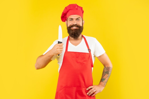 Homem feliz de avental vermelho e toque segurando fundo amarelo de faca de chef, chef