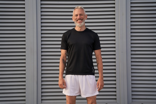 Homem feliz de meia idade em perfeita forma sorrindo para a câmera enquanto fica ao ar livre após o treino