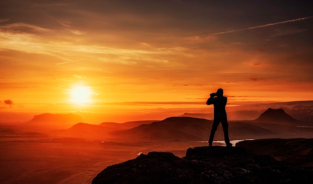 Homem feliz, de pé sobre um penhasco ao pôr do sol