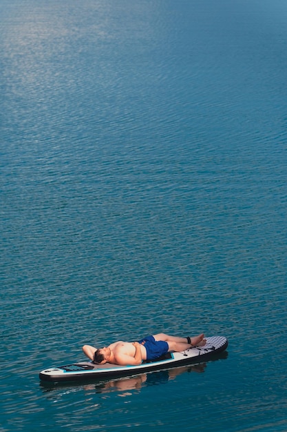 homem feliz deita-se em supboard banho de sol no meio do lago espaço de cópia