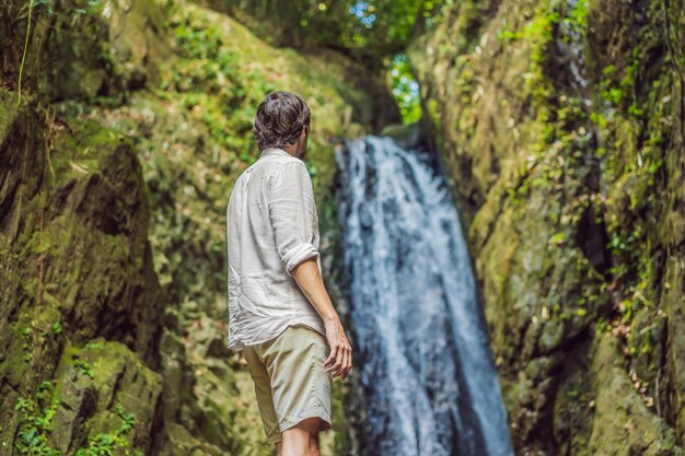 Homem feliz desfrutando de uma incrível cachoeira tropical levantou as mãos Estilo de vida de viagem e férias de conceito de sucesso na natureza selvagem na montanha de fundo