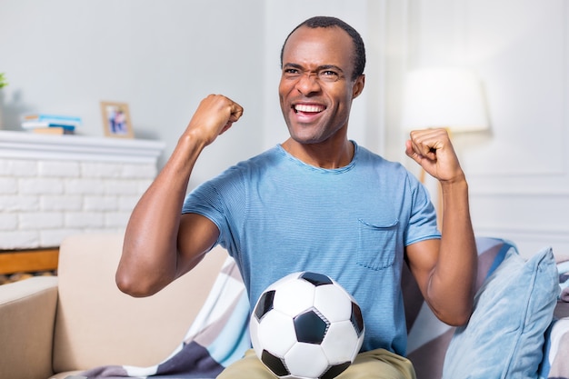 Homem feliz e alegre, sorrindo e segurando uma bola enquanto é fã de futebol