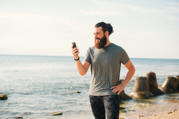 Homem feliz e desportivo está lendo uma mensagem no telefone enquanto faz uma pausa na corrida.