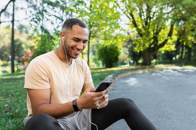 Foto homem feliz e satisfeito depois de fazer jogging e aula de fitness sentado e usando smartphone africano