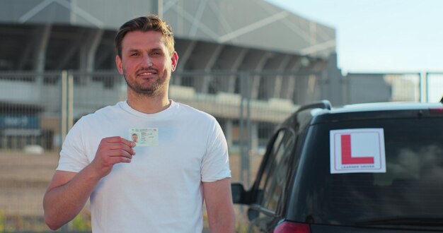 Homem feliz e sorridente, segurando carteira de motorista ao ar livre, exame de cursos de motorista e conceito de pessoas