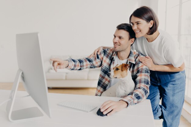 Homem feliz e sua namorada consultam sobre o projeto futuro, apontam para o monitor, posam no local de trabalho junto com o cachorro no interior da casa, assistem ao vídeo tutorial on-line, passam o tempo no apartamento moderno