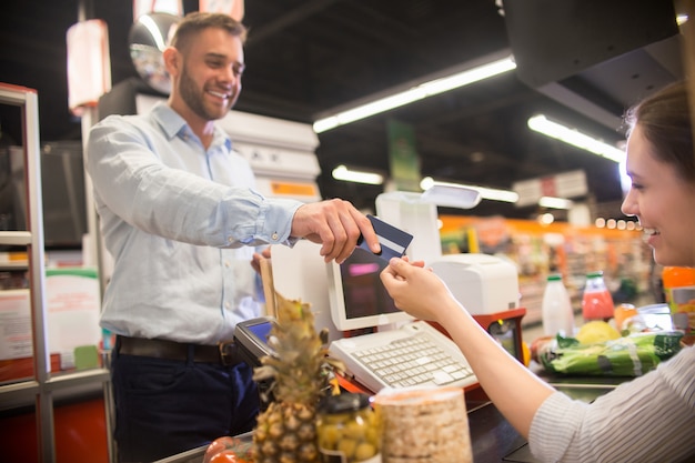 Homem feliz, entregando o cartão de crédito para caixa no supermercado