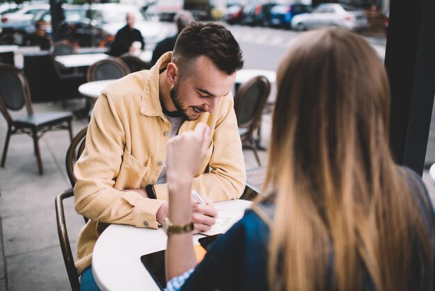 Foto homem feliz escrevendo no caderno enquanto conversa com mulher anônima