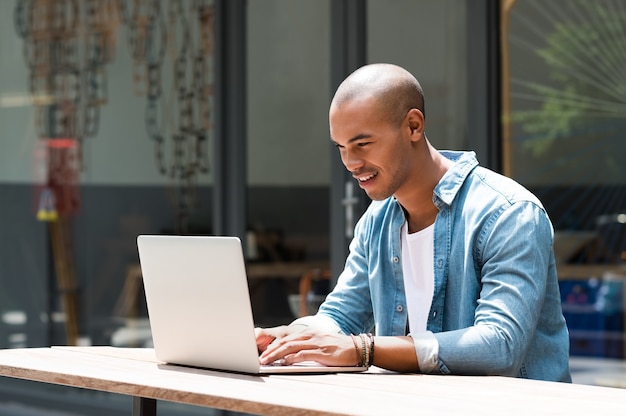 Homem feliz escrevendo um texto no laptop em uma cafeteria moderna