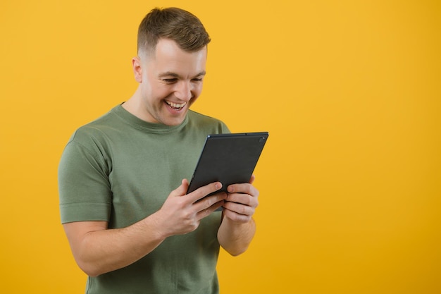 Homem feliz espantado usando tablet digital, parecendo chocado com as notícias da mídia social, consumidor de cliente espantado surpreso com a vitória online isolada sobre fundo amarelo.