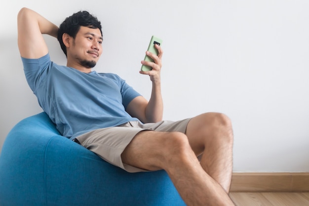 Homem feliz está usando o smartphone enquanto senta e relaxa sobre o saco de feijão.