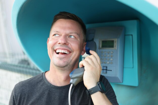 Homem feliz fala em um telefone público na rua closeup falta de telefone de conexão móvel