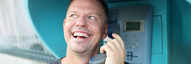 Homem feliz fala em um telefone público na rua closeup falta de telefone de conexão móvel