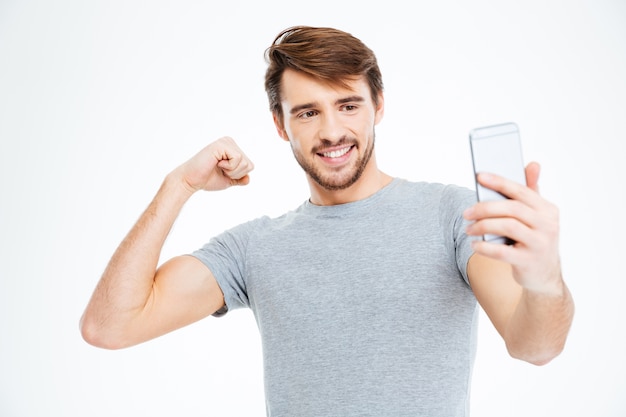 Homem feliz fazendo foto de selfie no smartphone e mostrando o bíceps isolado em um fundo branco