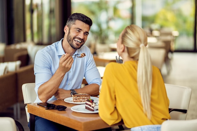 Homem feliz levando para sua namorada enquanto come bolo em um café