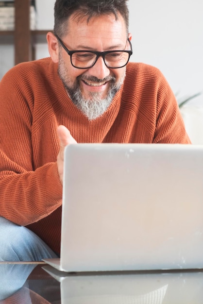 Homem feliz, maduro e bonito sentado no sofá enquanto faz uma videochamada com um laptop Online empresário de pequenas empresas fazendo uma videoconferência usando óculos enquanto trabalha em casa novo conceito normal