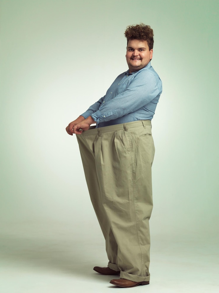 Foto homem feliz mais tamanho e perda de peso com calças para medição ou cintura em um fundo de estúdio pessoa masculina com sorriso para dieta saudável nutrição e oversize na moda ou roupas em espaço de maquete