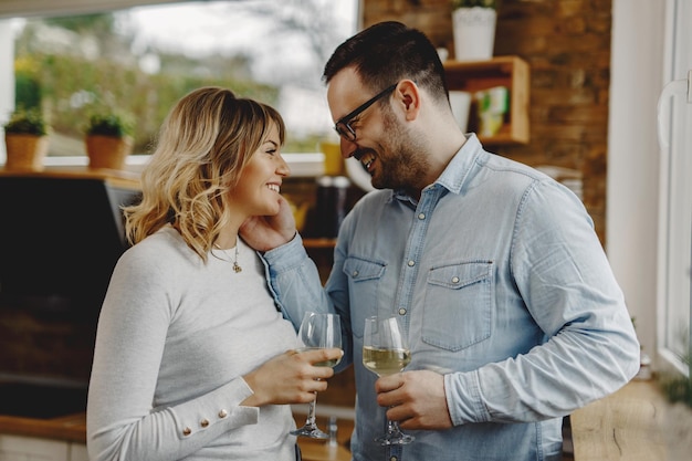 Foto homem feliz mostrando carinho enquanto se comunica com sua esposa e bebe vinho na cozinha