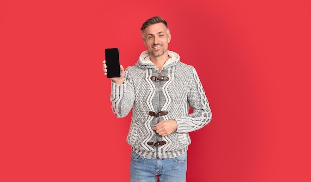 Homem feliz na camisola mostrando a tela do telefone em fundo vermelho com anúncio de espaço de cópia