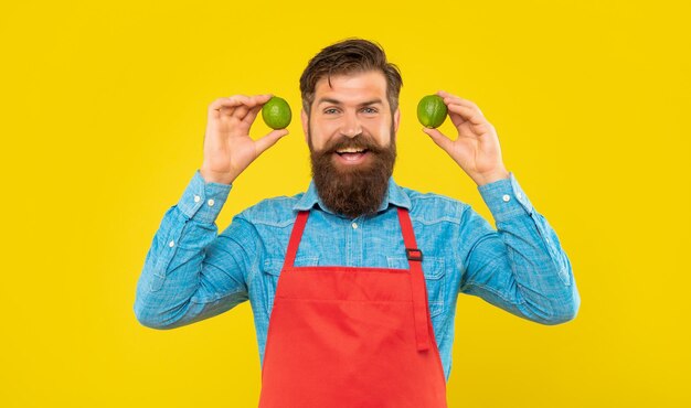 Homem feliz no avental vermelho segurando limões frescos frutas cítricas fundo amarelo verdureiro