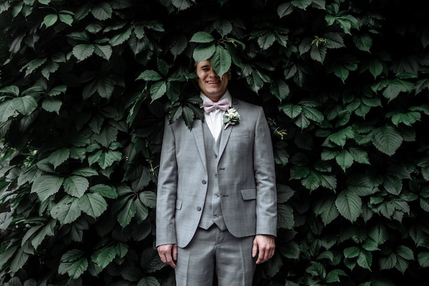 Foto homem feliz noivo em terno de casamento no dia do casamento no jardim na parede de ivy