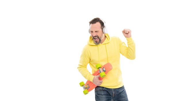 Homem feliz ouve música em fones de ouvido segura skate de centavo isolado na atividade de espaço de cópia branca