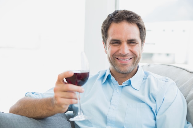 Homem feliz relaxando no sofá com um copo de vinho tinto